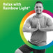 A young man smiling while doing yoga, illuminated by a rainbow light in a peaceful setting.