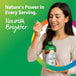 A woman smiles while tasting liquid from a spoon, holding a Pumpkin Seed Oil bottle.